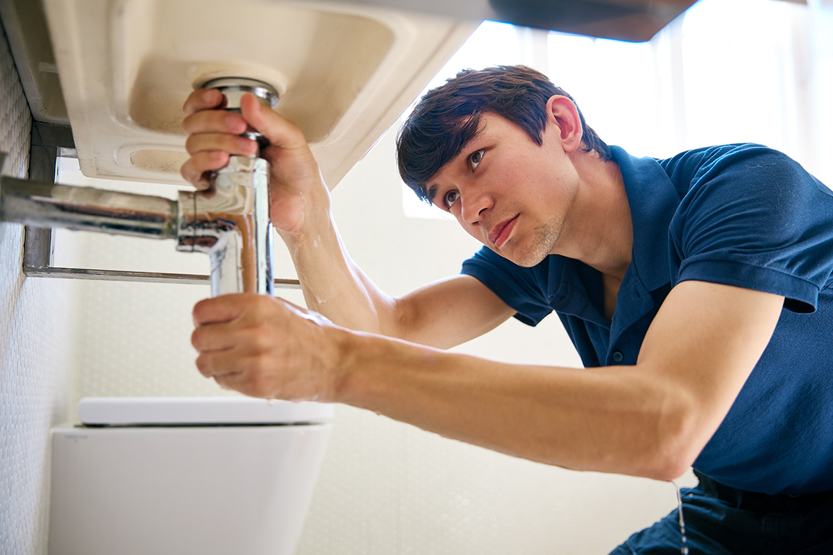 Male Plumber Fixing Leak In Domestic Bathroom Sink Or Basin